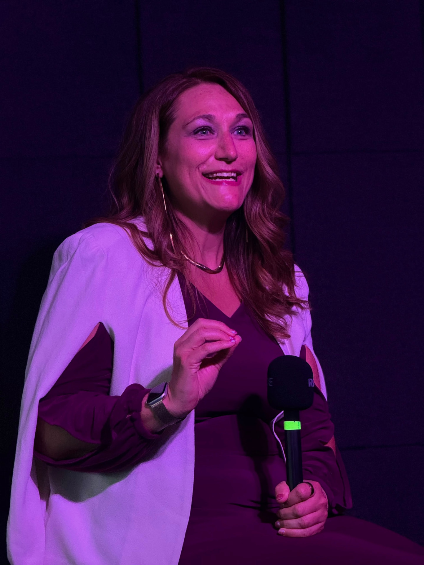 Joy St. John speaking on stage with a handheld microphone